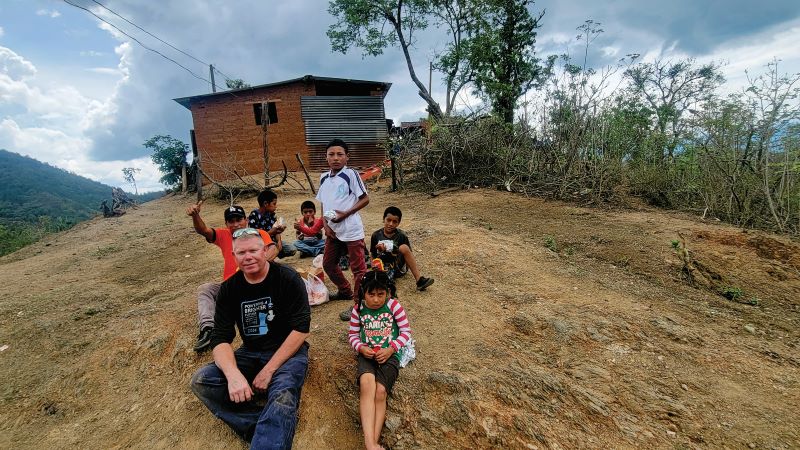 Brian Reidy with 5 Guatemalan kids and a villager sitting in front of a house